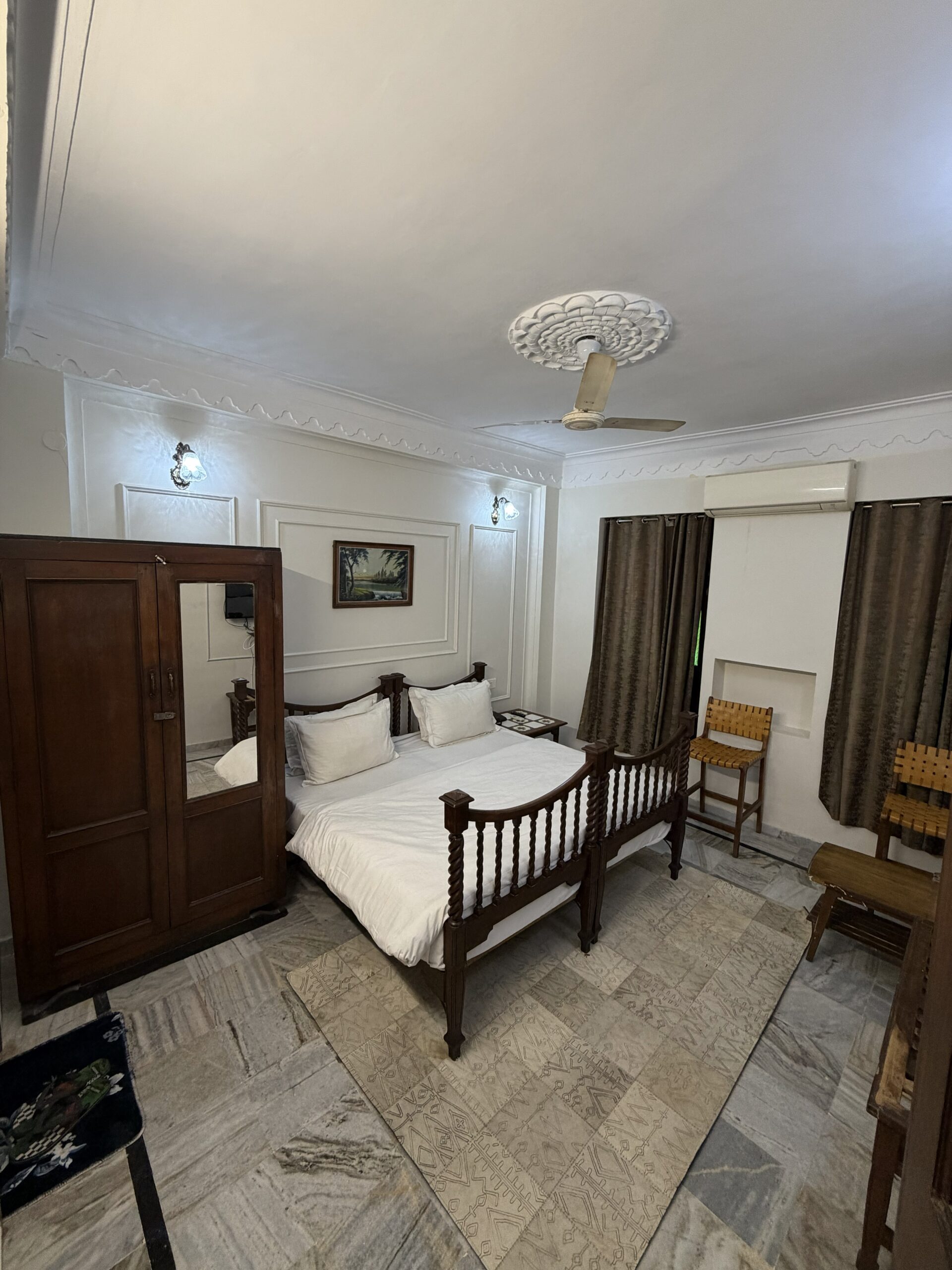 Heritage-style deluxe room at Hotel Royale Plazo Jodhpur showing wooden bed, open jharokha windows, white walls and comfortable bedding