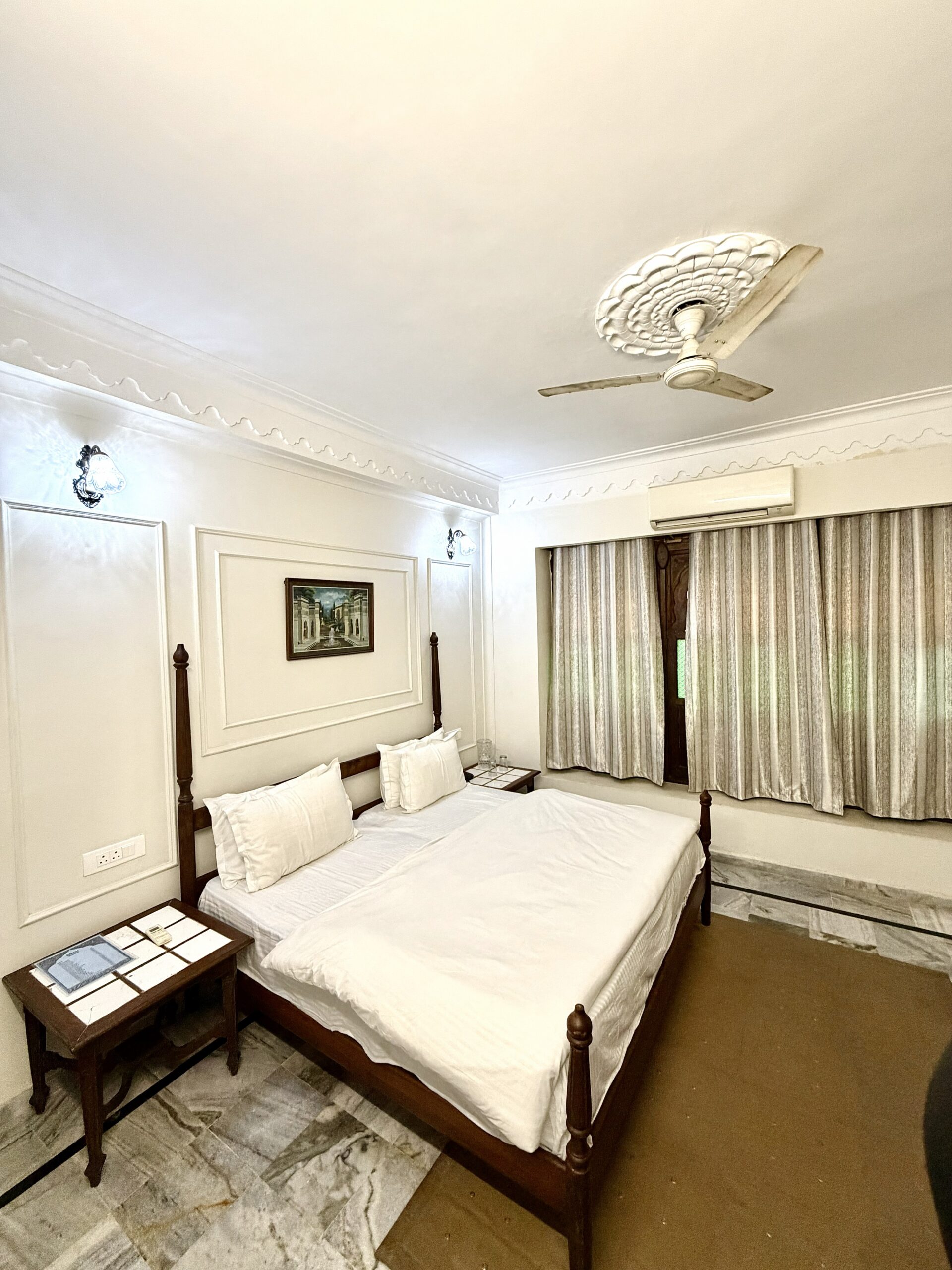 Executive Room at Hotel Royale Plazo Jodhpur with large wooden bed, premium white linens, elegant wall decor, ceiling design, and natural light through curtains
