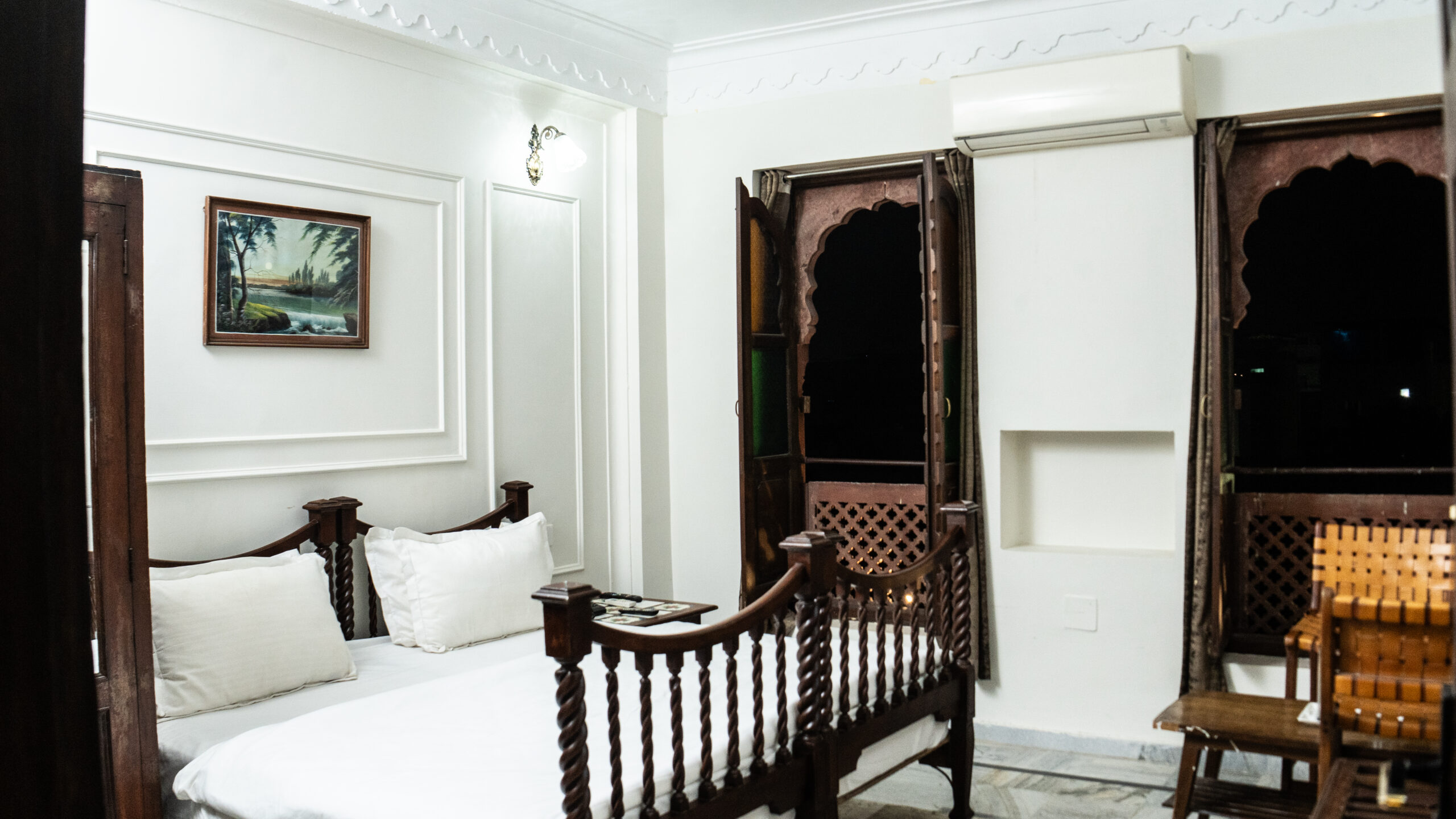 Heritage-style deluxe room at Hotel Royale Plazo Jodhpur showing wooden bed, open jharokha windows, white walls and comfortable bedding
